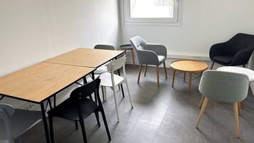 Una habitación con una mesa de madera, sillas blancas y negras, un sillón gris y un sillón negro, además de una mesa redonda de madera.