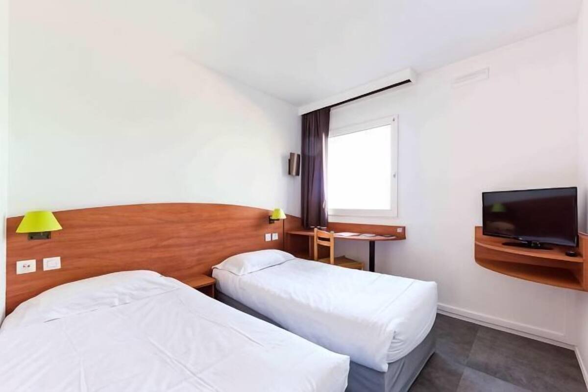 A hotel room with two beds, a desk with a chair, a television, and a window.