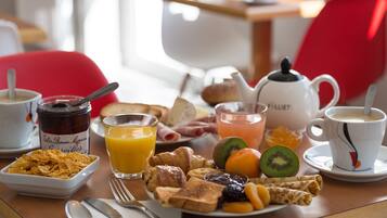 A breakfast table with cereal, juice, croissants, fruits, and a teapot.