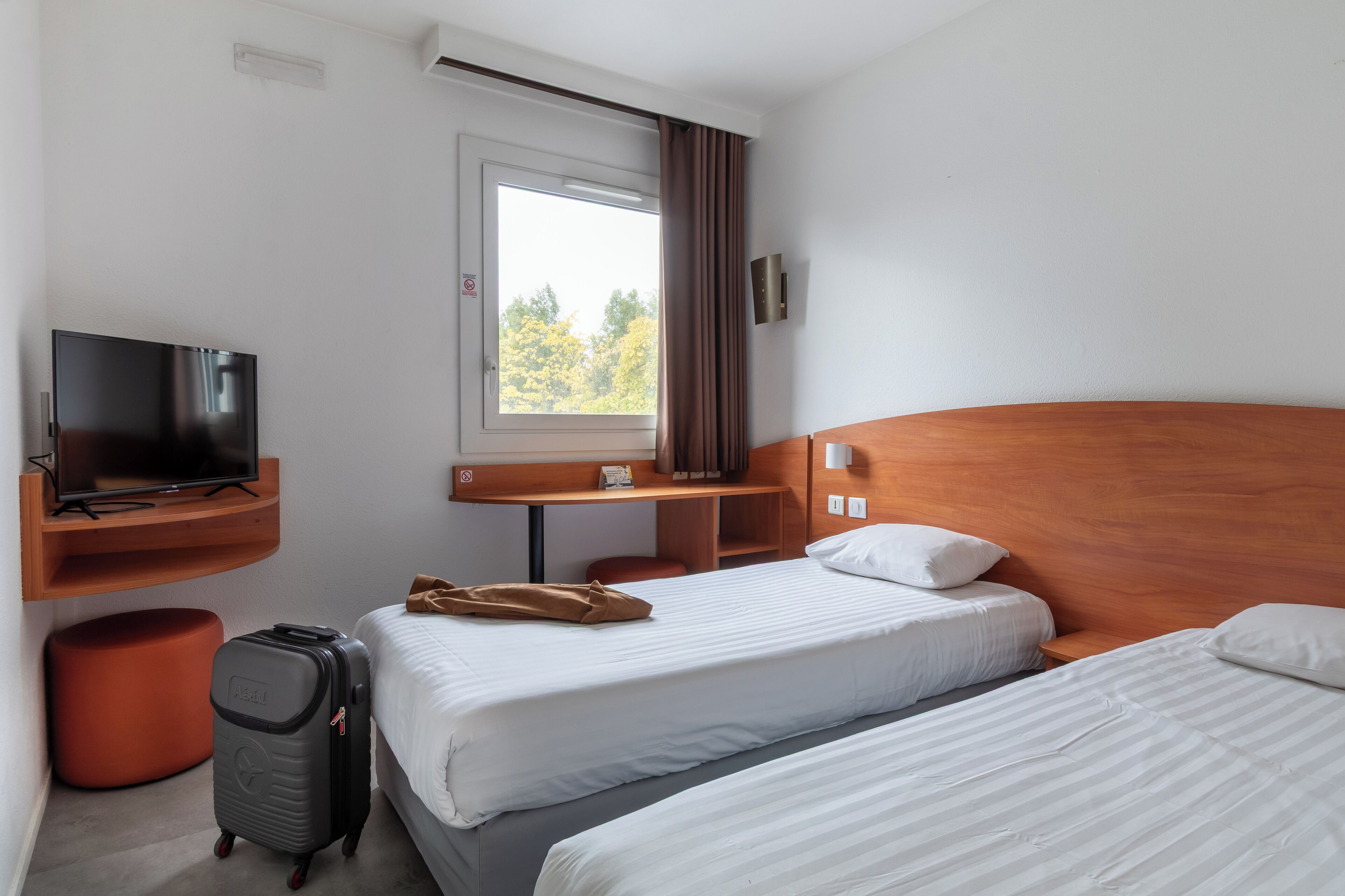 Habitación de hotel con dos camas, televisión, escritorio y ventana con cortinas.