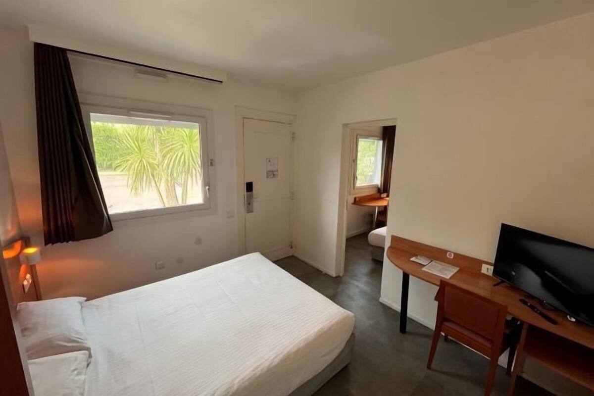 Een hotelkamer met een bed, bureau, televisie en een raam met gordijnen.
