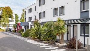 Un edificio moderno con facciata pulita, numerose finestre e un giardino curato con diverse piante.