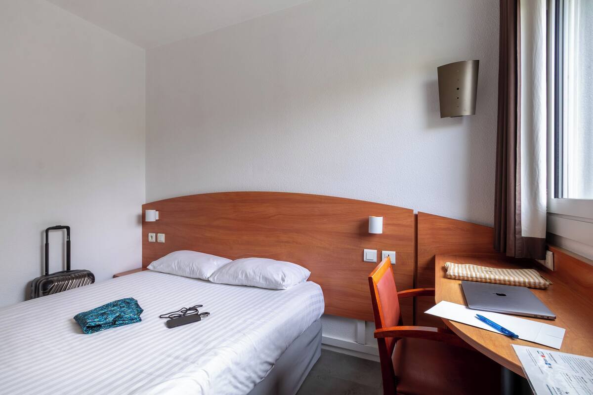 Een hotelkamer met een bed, een bureau met een laptop, een koffer en een stoel.