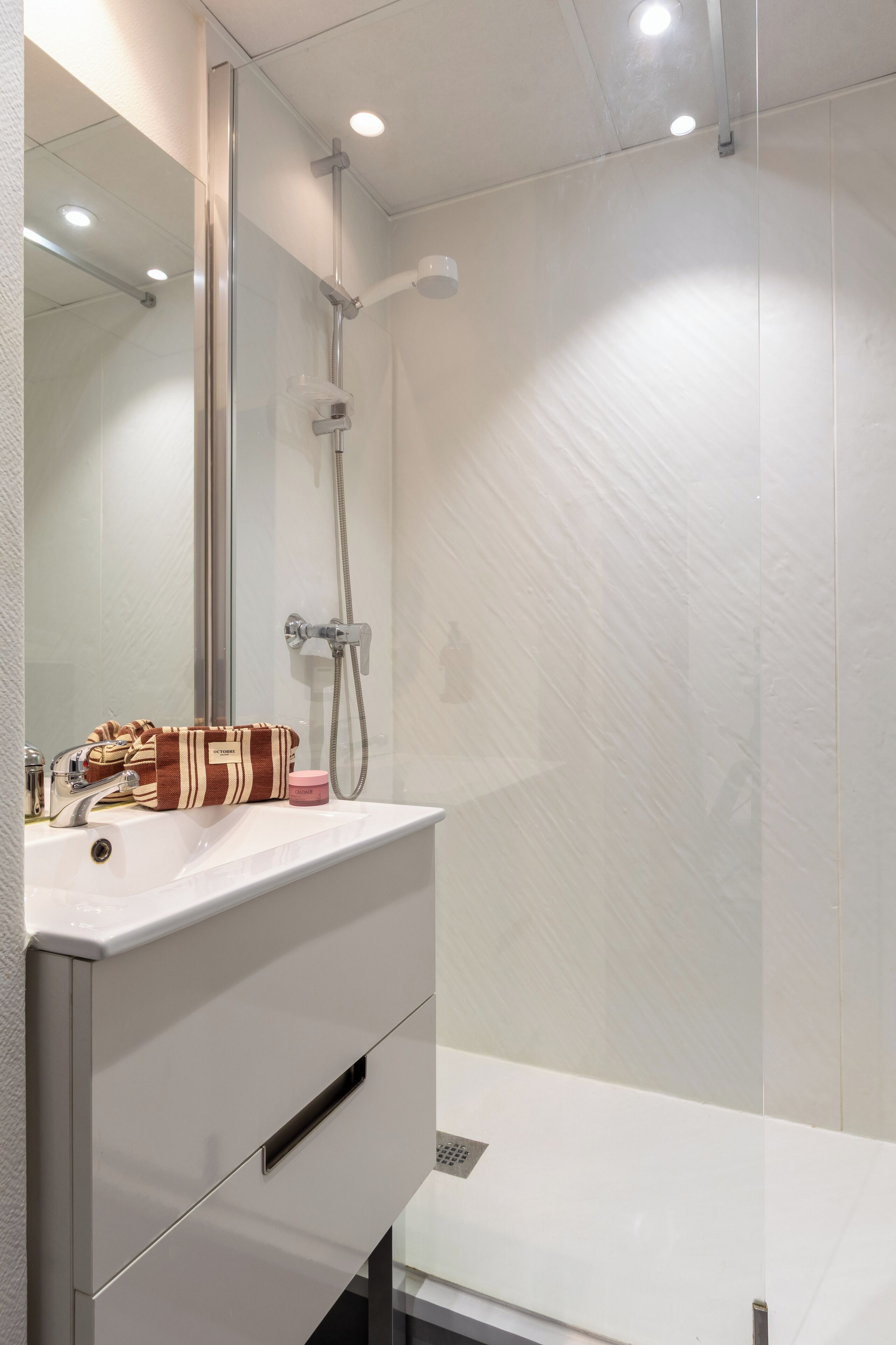 A modern bathroom with a white vanity, a shower with a handheld showerhead, and a mirror above the vanity.