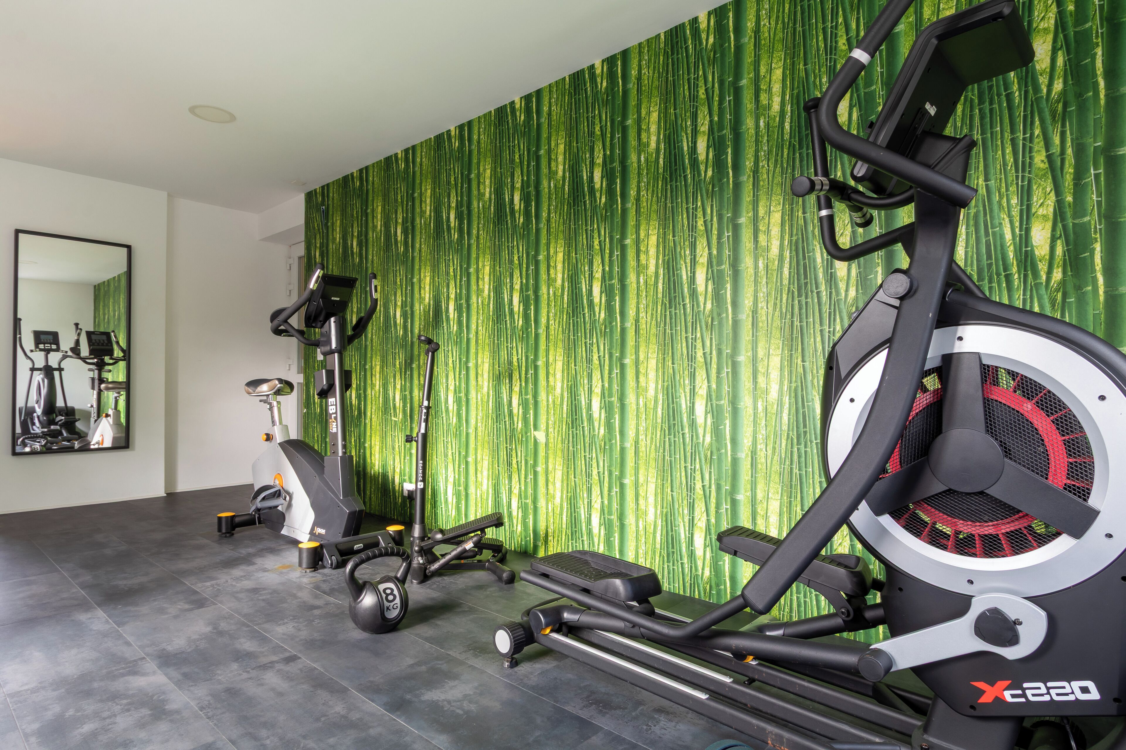 A home gym with stationary bikes, a treadmill, and a rowing machine against a green bamboo wallpaper.