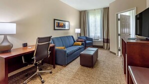 A hotel room with a desk, two sofas, a TV, and a window with curtains. - Comfort Suites Clarksville near Governors Square Mall (Clarksville)