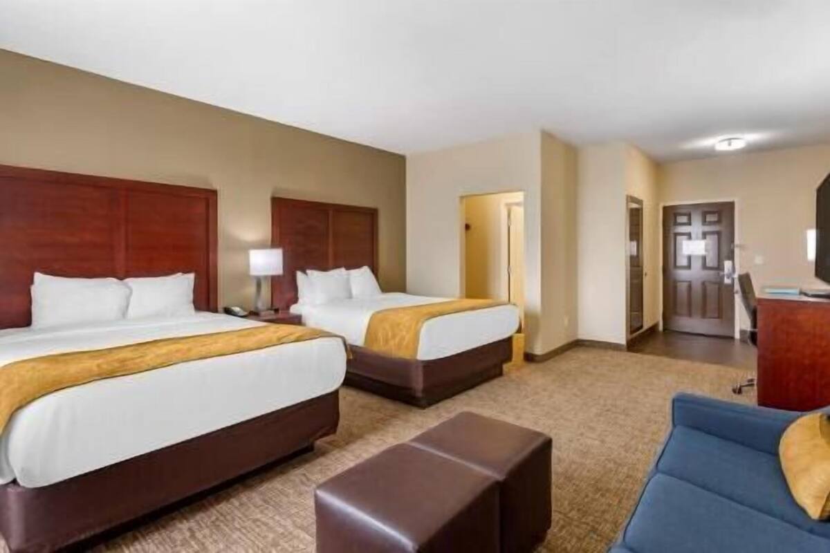 A hotel room with two beds, a desk, a chair, and a small sofa.