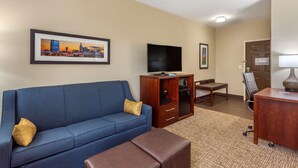 A hotel room with a blue sofa, a TV, a wooden cabinet, a desk, and a chair. - Comfort Suites Clarksville near Governors Square Mall (Clarksville)