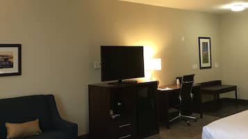 Habitación de hotel con dos camas, un escritorio con computadora, televisor, lámpara y sofá.