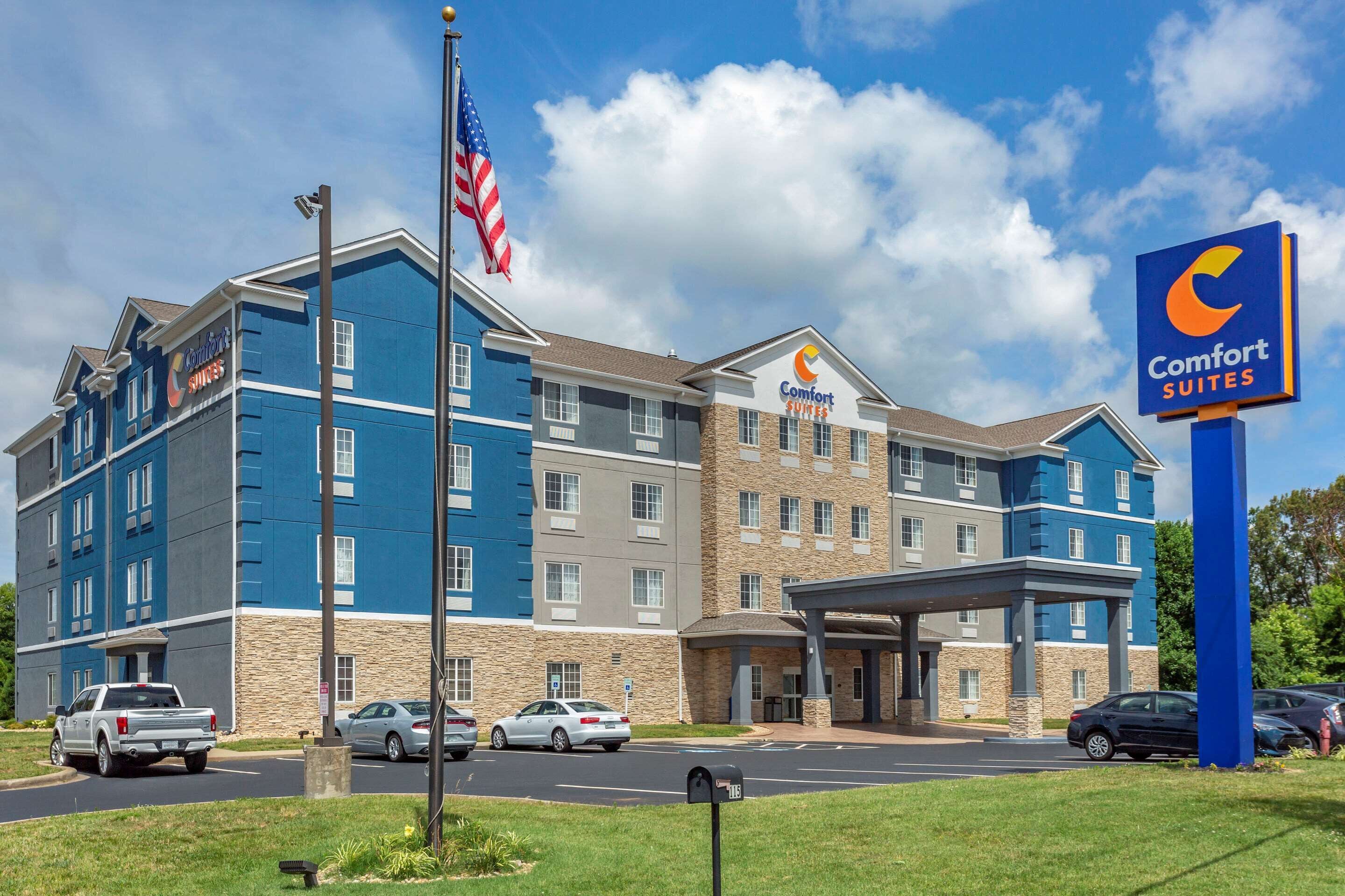 A Comfort Suites hotel with a blue and beige exterior, multiple floors, and a covered entrance.