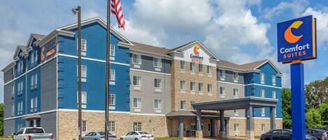 A Comfort Suites hotel with a blue and beige exterior, multiple floors, and a covered entrance.