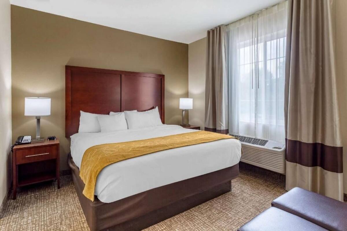 A hotel room with a large bed, two bedside tables, a heater, and a window with curtains.