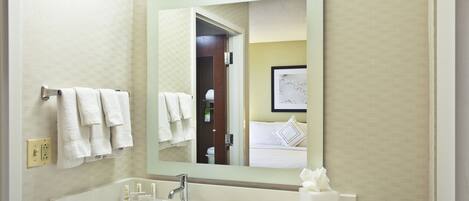 Un baño de hotel con un espejo grande, toallas blancas, un lavamanos y un cuadro enmarcado en la pared.