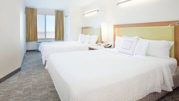 Une chambre d’hôtel avec deux lits, une fenêtre avec des rideaux, une table de chevet avec une lampe et un téléphone fixé au mur.