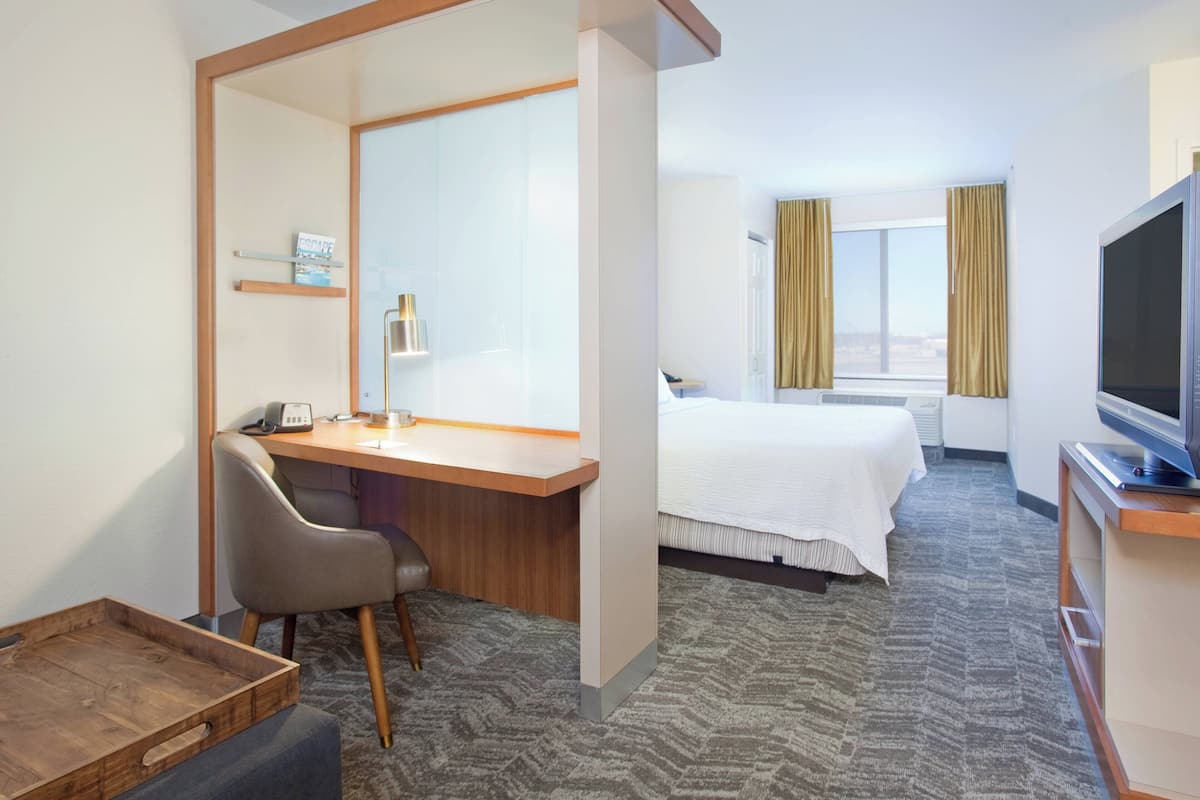 A hotel room with a desk, chair, bed, television, and a window with curtains.