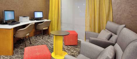 A hotel room with two desks, two chairs, a sofa, a small table, and a large window with yellow curtains.