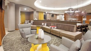 A modern hotel lobby with a curved seating area, a reception desk, and a bar. - SpringHill Suites by Marriott Wichita East at Plazzio (Wichita)
