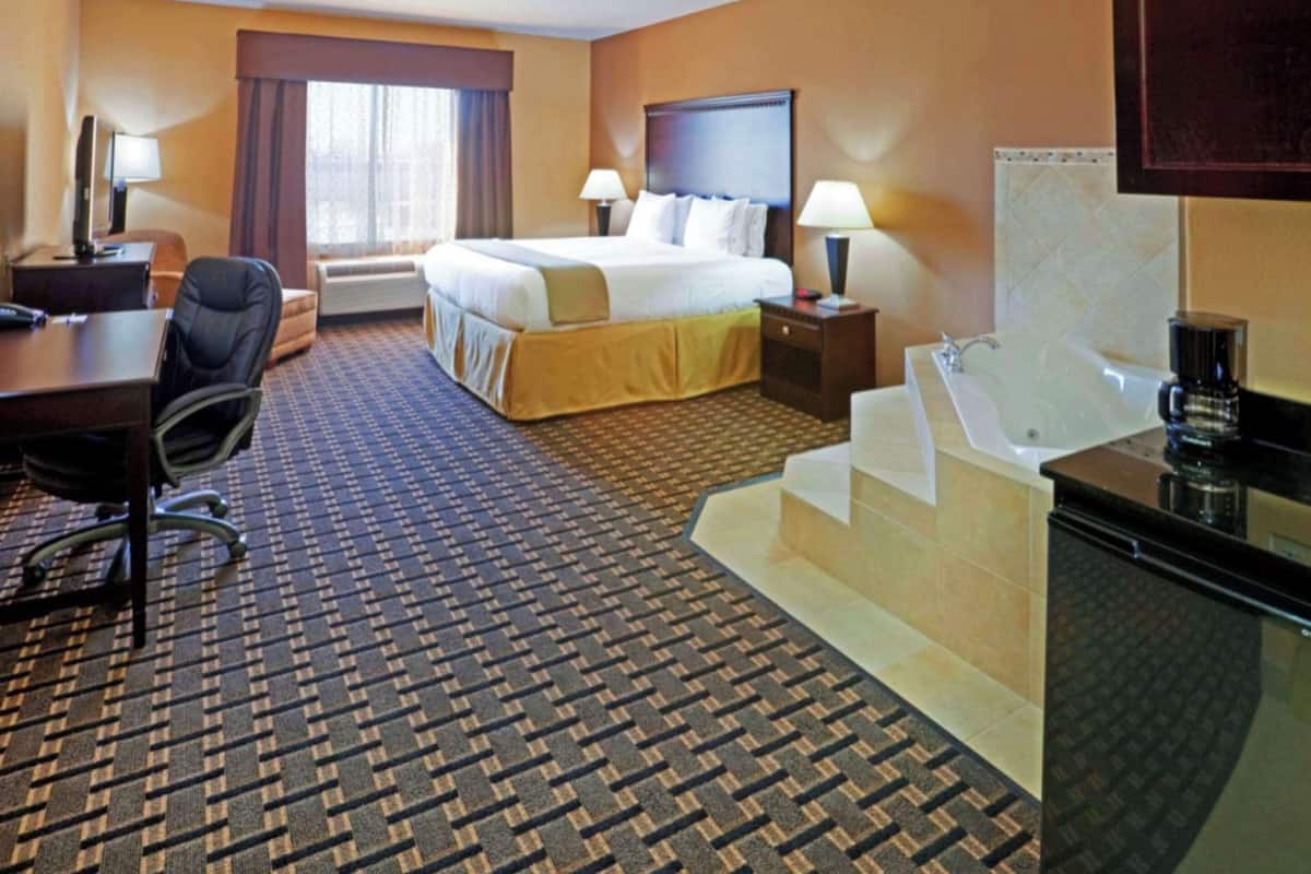 Ein Hotelzimmer mit Bett, Schreibtisch, Stuhl, Lampe und Badewanne.