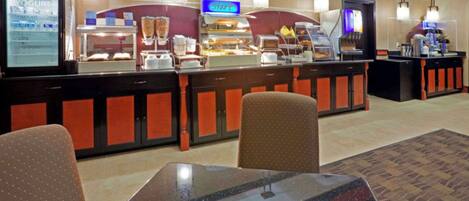 A hotel breakfast area with a self-service counter, seating, and a yogurt machine.