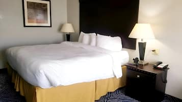 A neatly made bed with white linens, a dark headboard, and a patterned carpet. There are two bedside lamps and a phone on a nightstand.