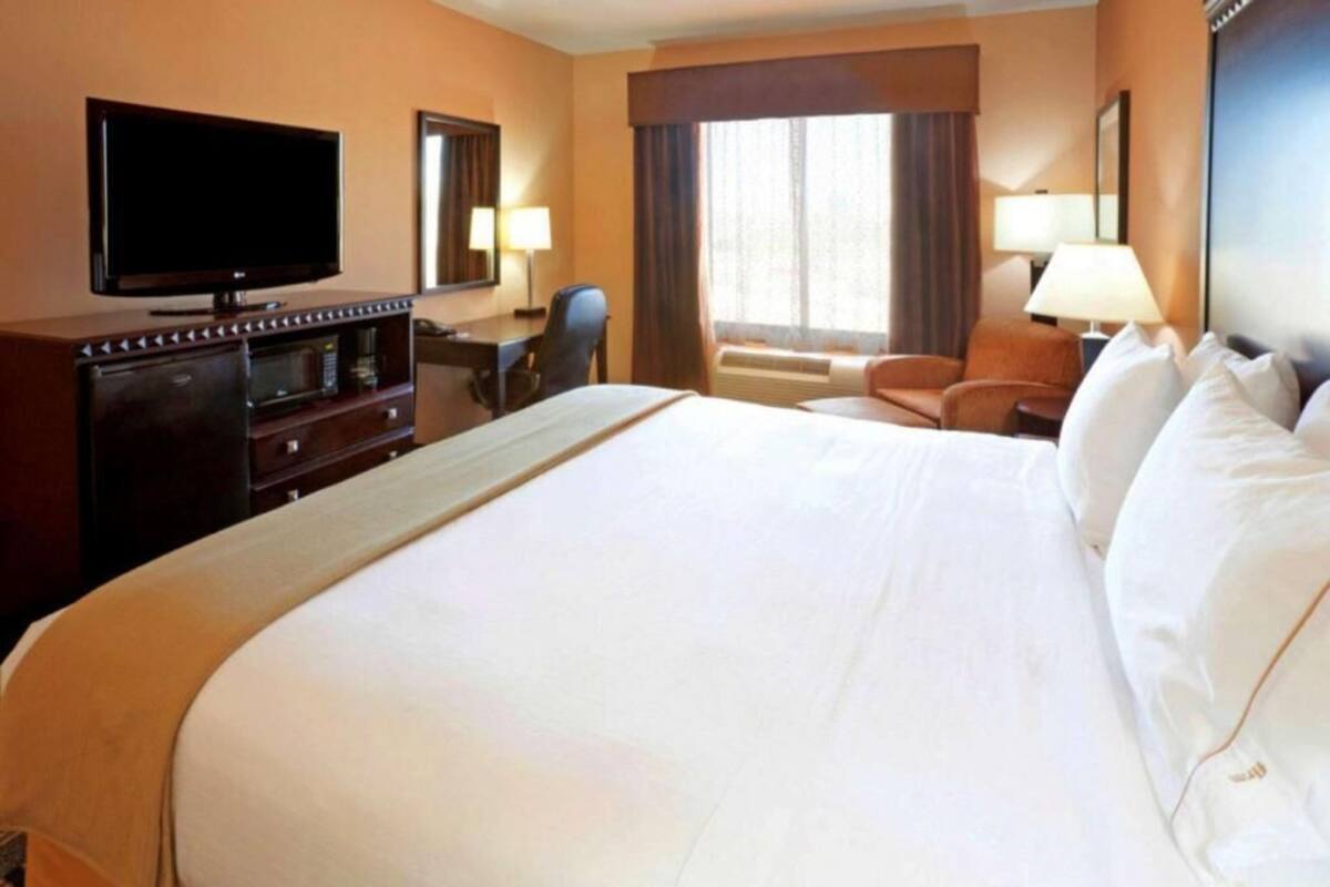 Ein Hotelzimmer mit einem großen Bett, einem Fernseher, einem Schreibtisch mit Stuhl und einem Vorhangfenster.