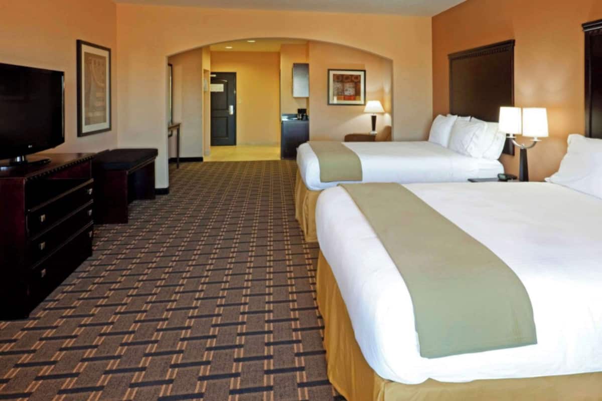 Ein Hotelzimmer mit zwei Betten, einem Fernseher, einem Schreibtisch und Teppichboden.