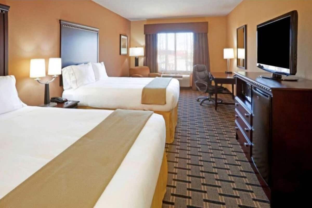 Ein Hotelzimmer mit zwei Betten, einem Schreibtisch, einem Fernseher und einem Sessel.