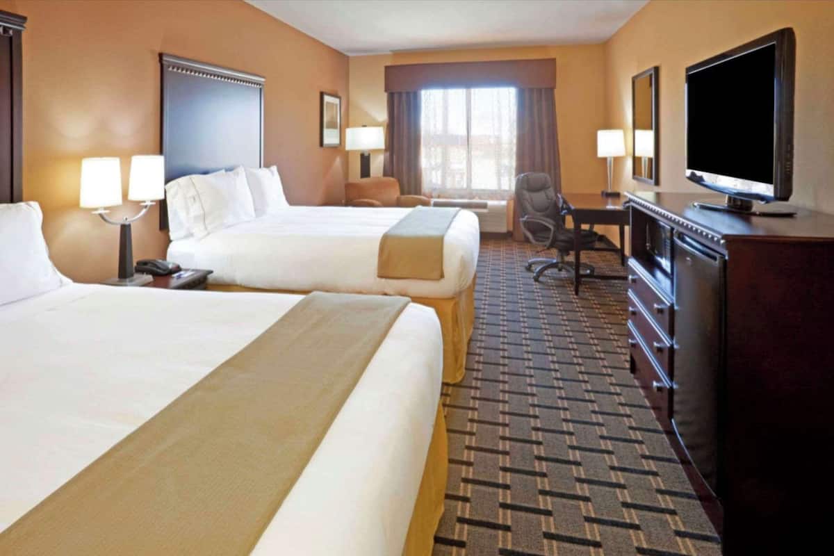 Ein Hotelzimmer mit zwei Betten, einem Schreibtisch, einem Fernseher und einem Sessel.
