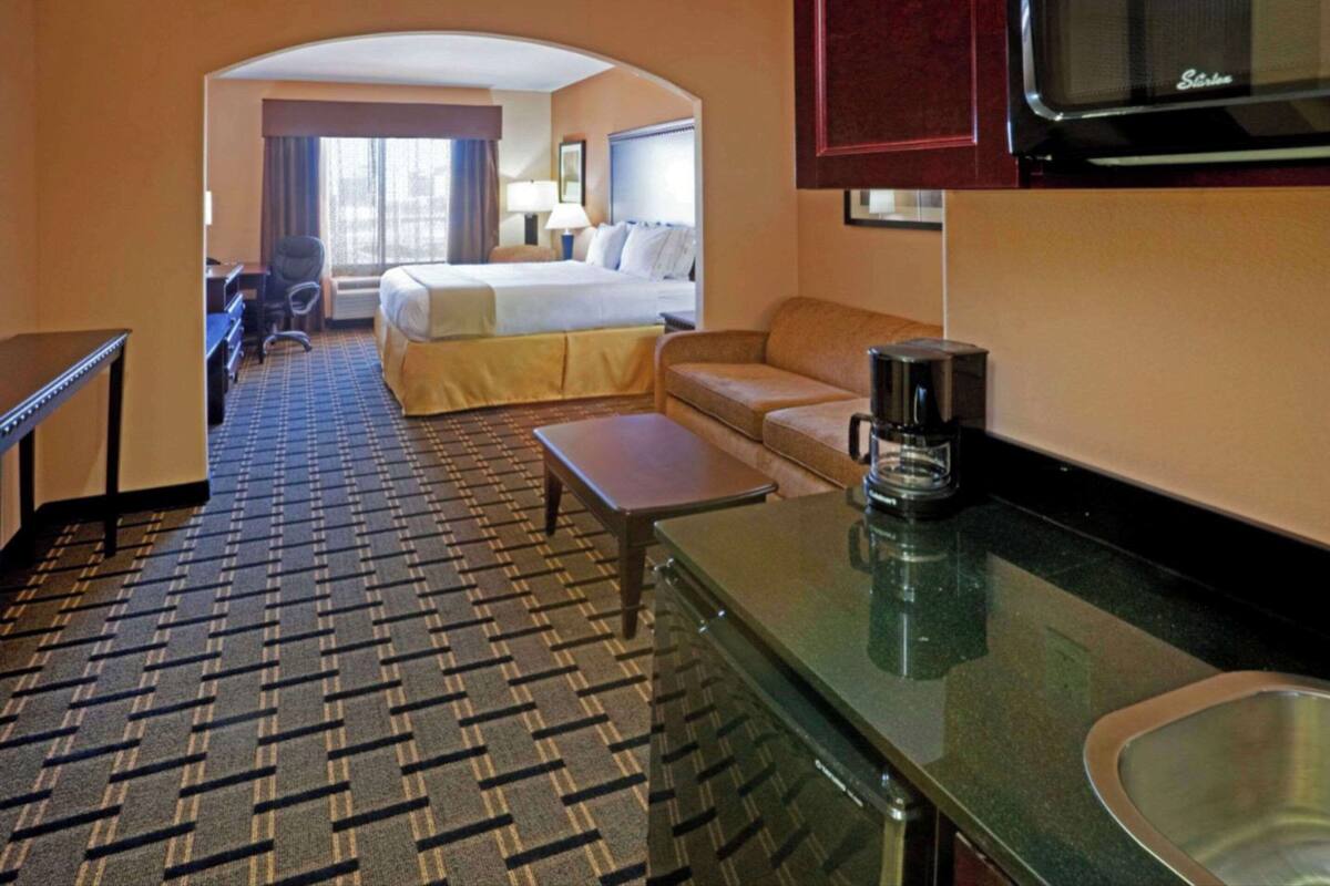 Ein Hotelzimmer mit Bett, einer Sitzecke, einer Kaffeemaschine, einem Schreibtisch und einer Küchenzeile.