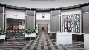 En modern hotellobby med ett rutmönstrat golv, en receptionsdisk och ett receptionsområde med en stor, abstrakt målning.