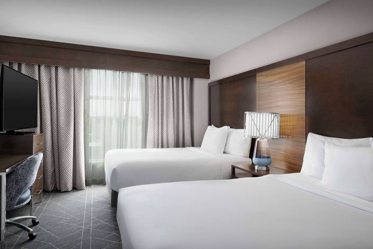 Ein Hotelzimmer mit zwei Betten, einem Schreibtisch, einem Stuhl, einem Fernseher und einer Lampe.