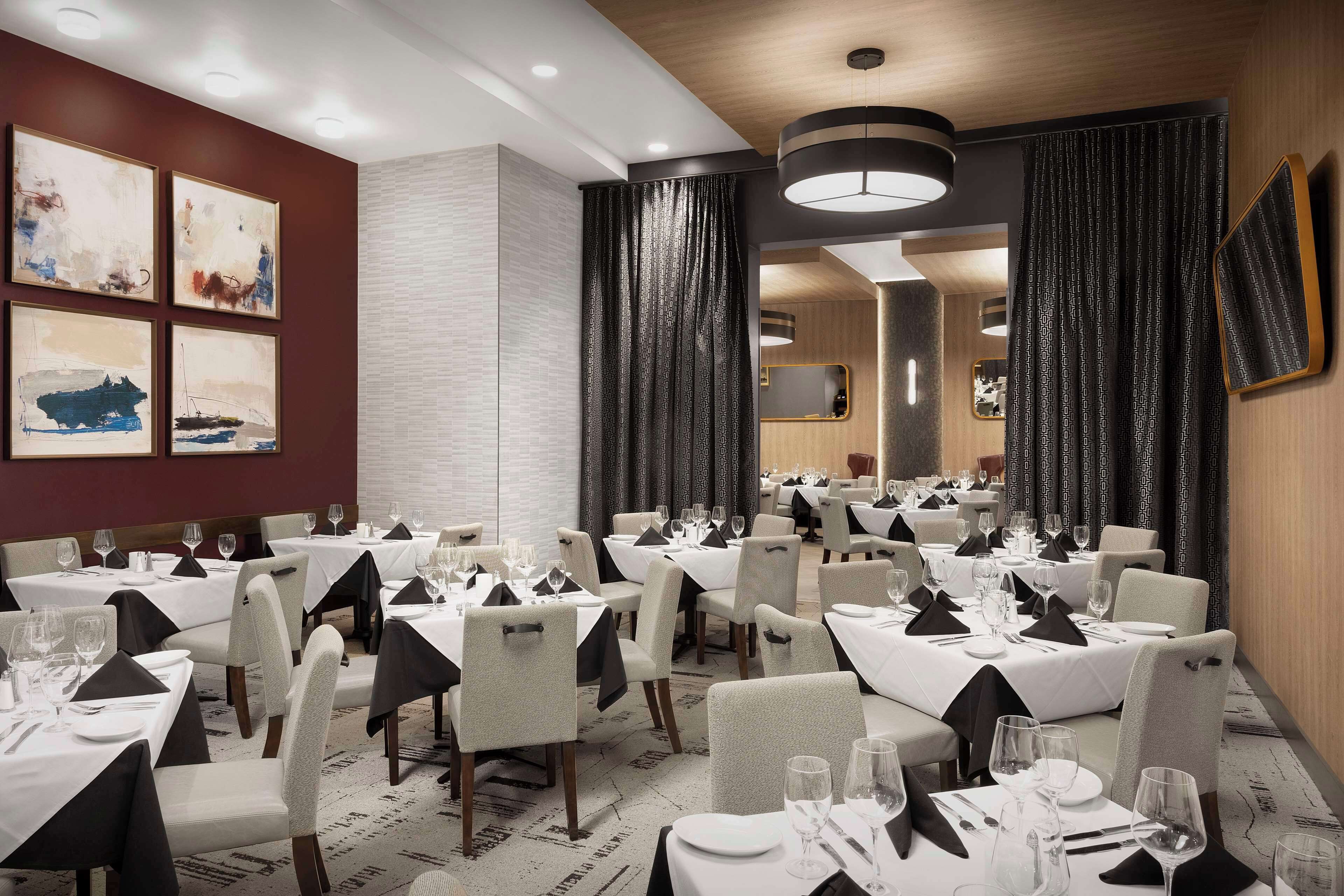 Un comedor con mesas dispuestas para el servicio, un espejo grande y obras de arte en las paredes.