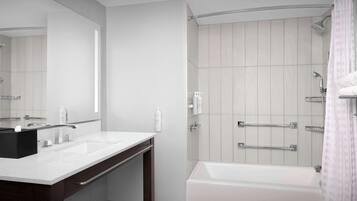 Un baño moderno con un espejo grande, dos lavamanos, una bañera y una ducha con barras de apoyo.