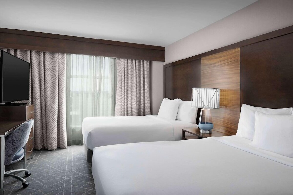 Une chambre d’hôtel avec deux lits, un bureau, une chaise, une télévision et une lampe.