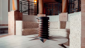 Eine Lobby mit einer zentralen Säule, gefliesten Wänden und einem dekorativen Metallgeländer.