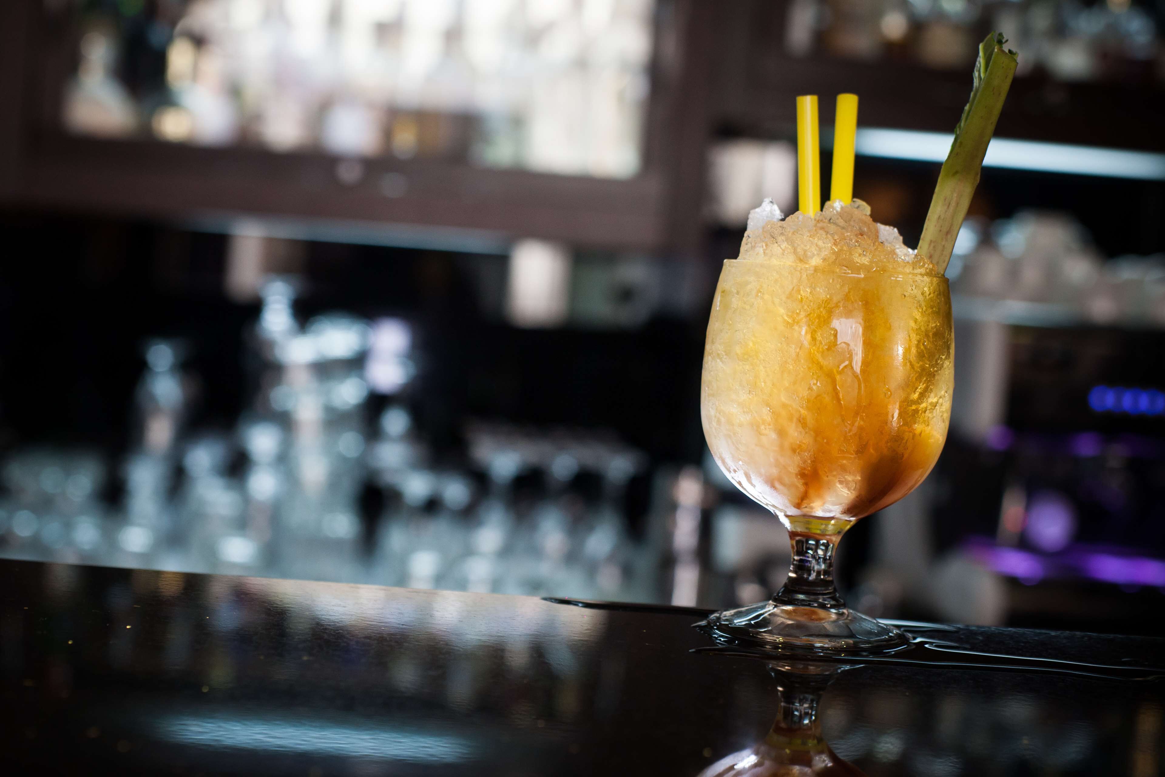 A cocktail with a straw and a decorative stick in a glass on a bar counter.