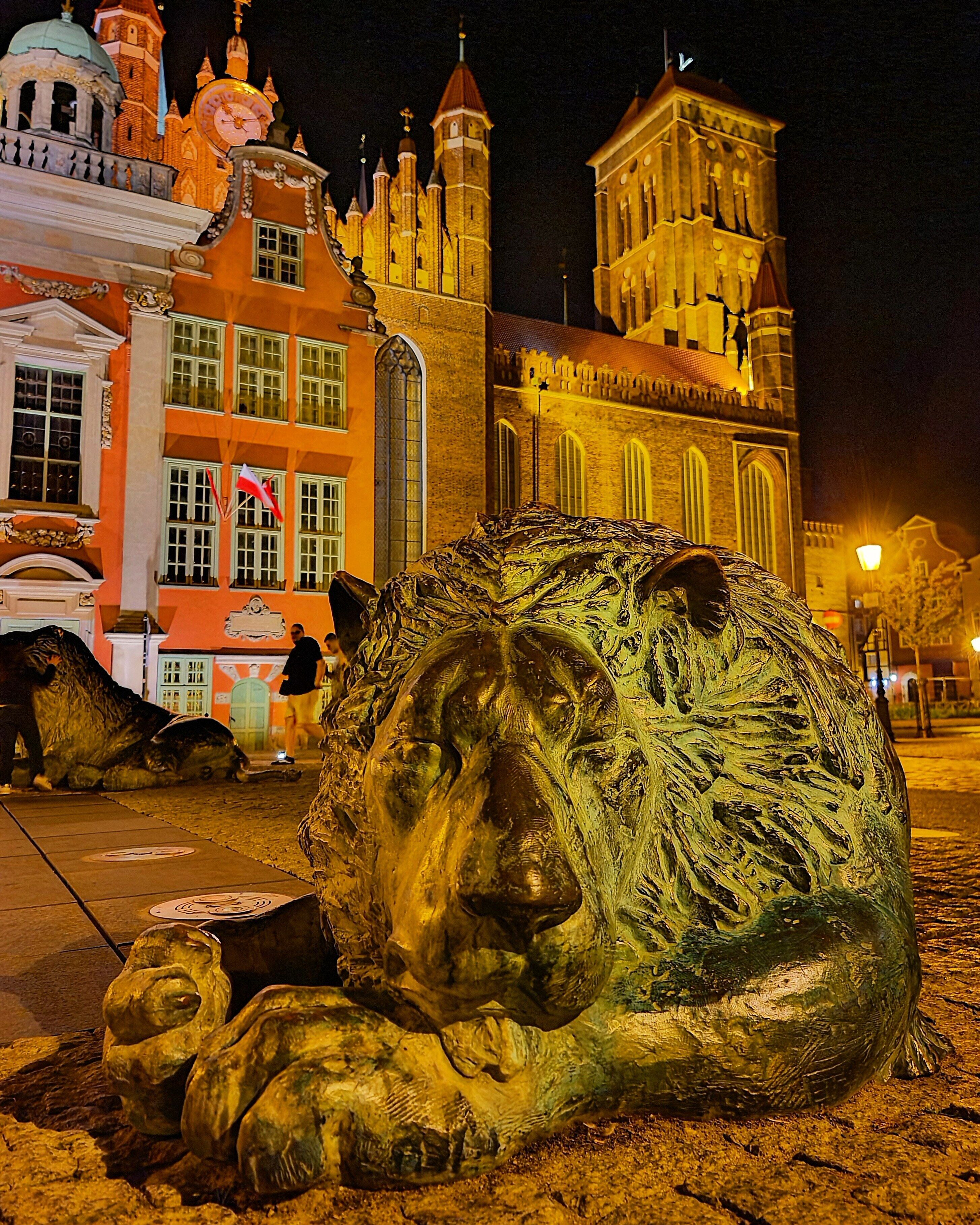 A large bronze lion sculpture in an outdoor urban setting at night.