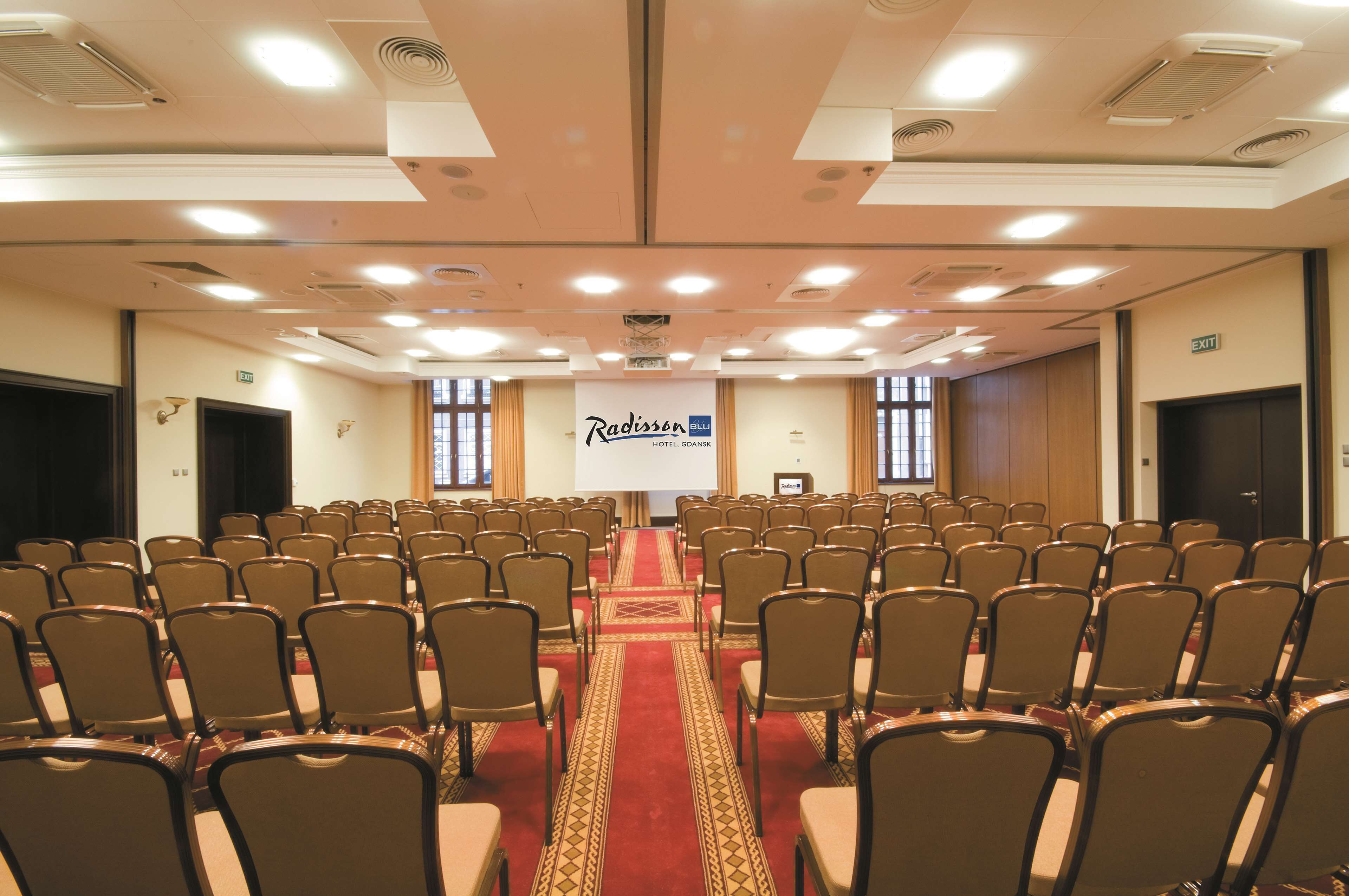 A conference room with rows of chairs, a red carpet, and a Radisson Blu sign.