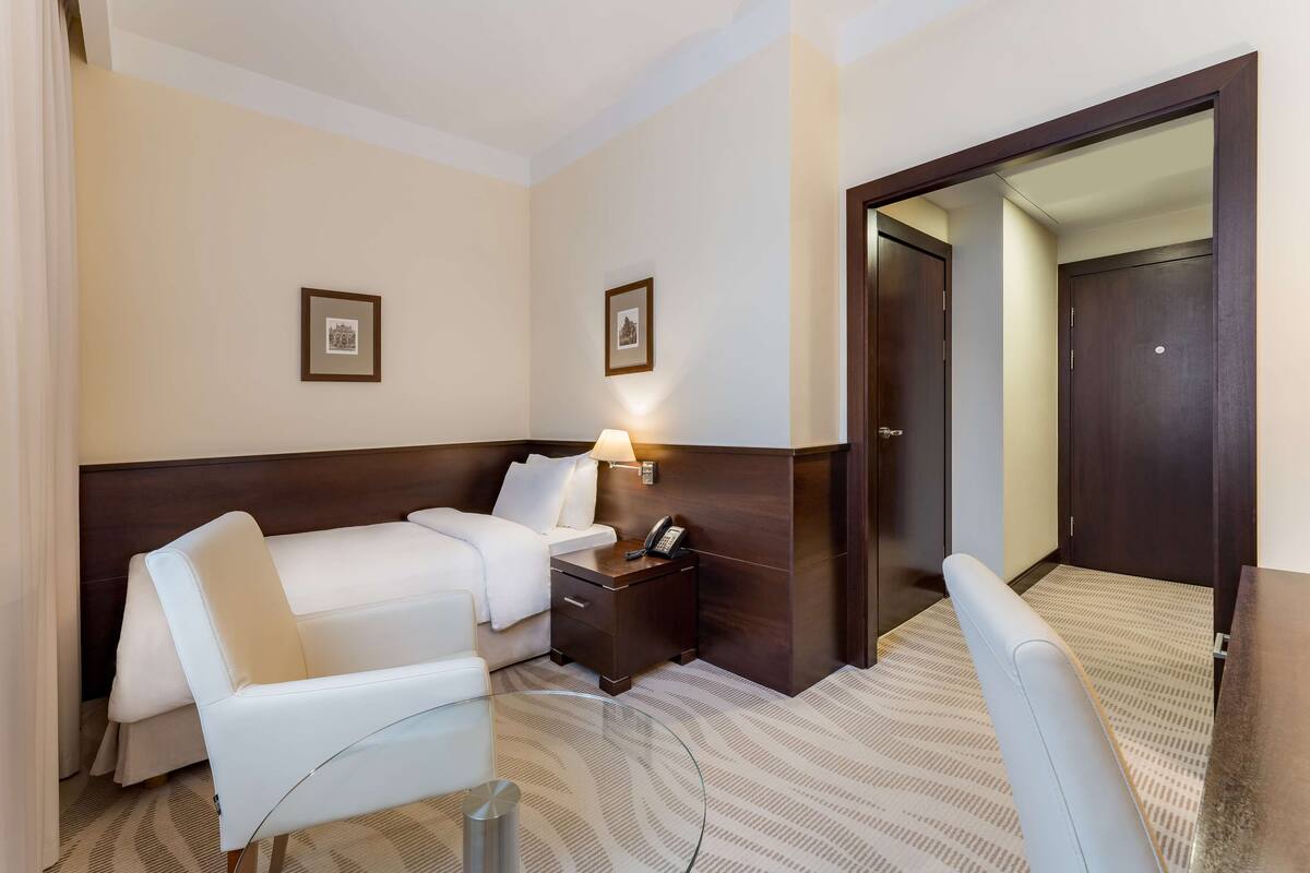 A hotel room with a bed, a desk with a lamp, a chair, and a large mirror.