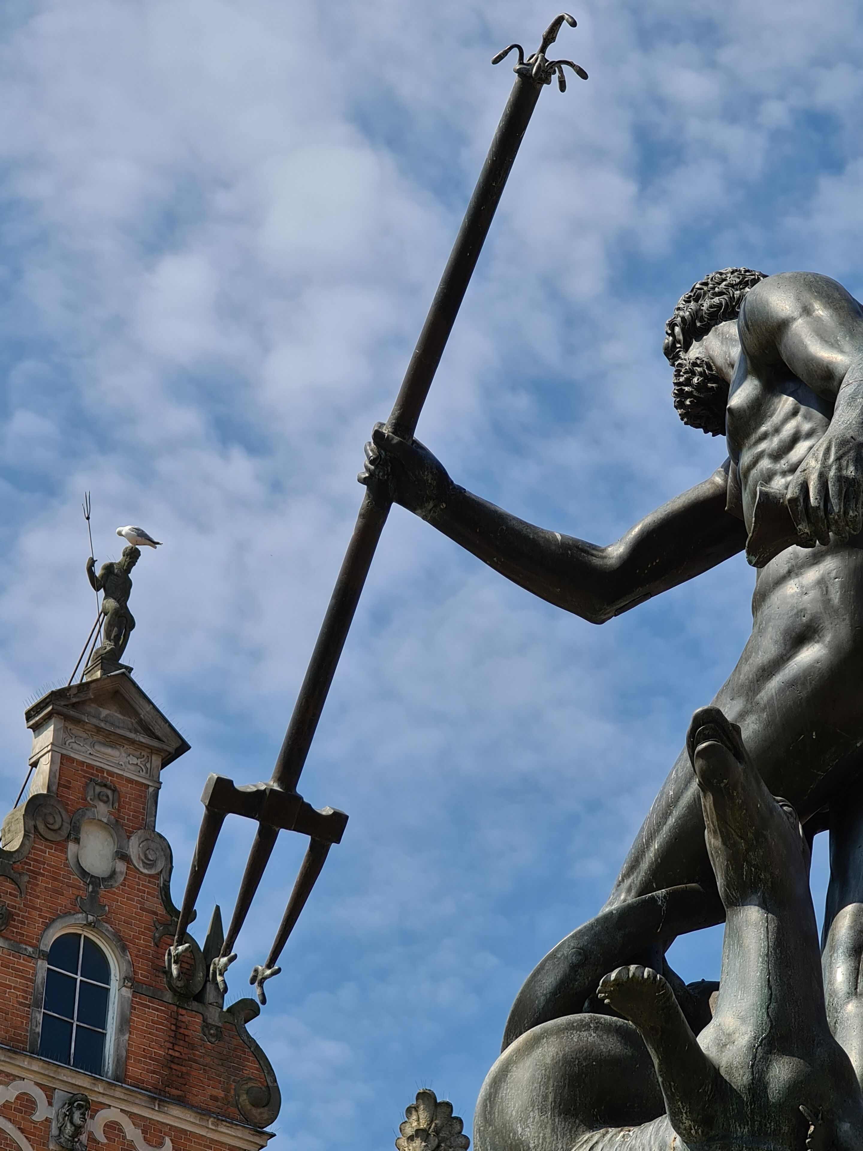 En staty av en muskulös man som håller ett trefjäll, med en klarblå himmel som bakgrund.