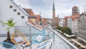 A rooftop terrace with wicker chairs, a small table with a plate of food, and a view of historic buildings and a clock tower.