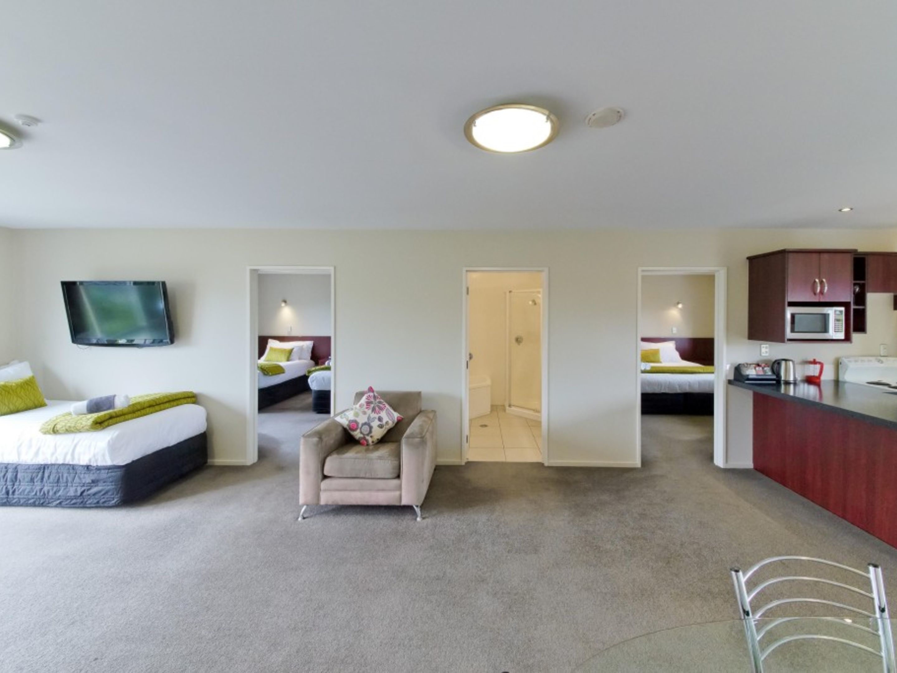 Habitación de hotel con cama, una silla, televisión, ducha y kitchenette.