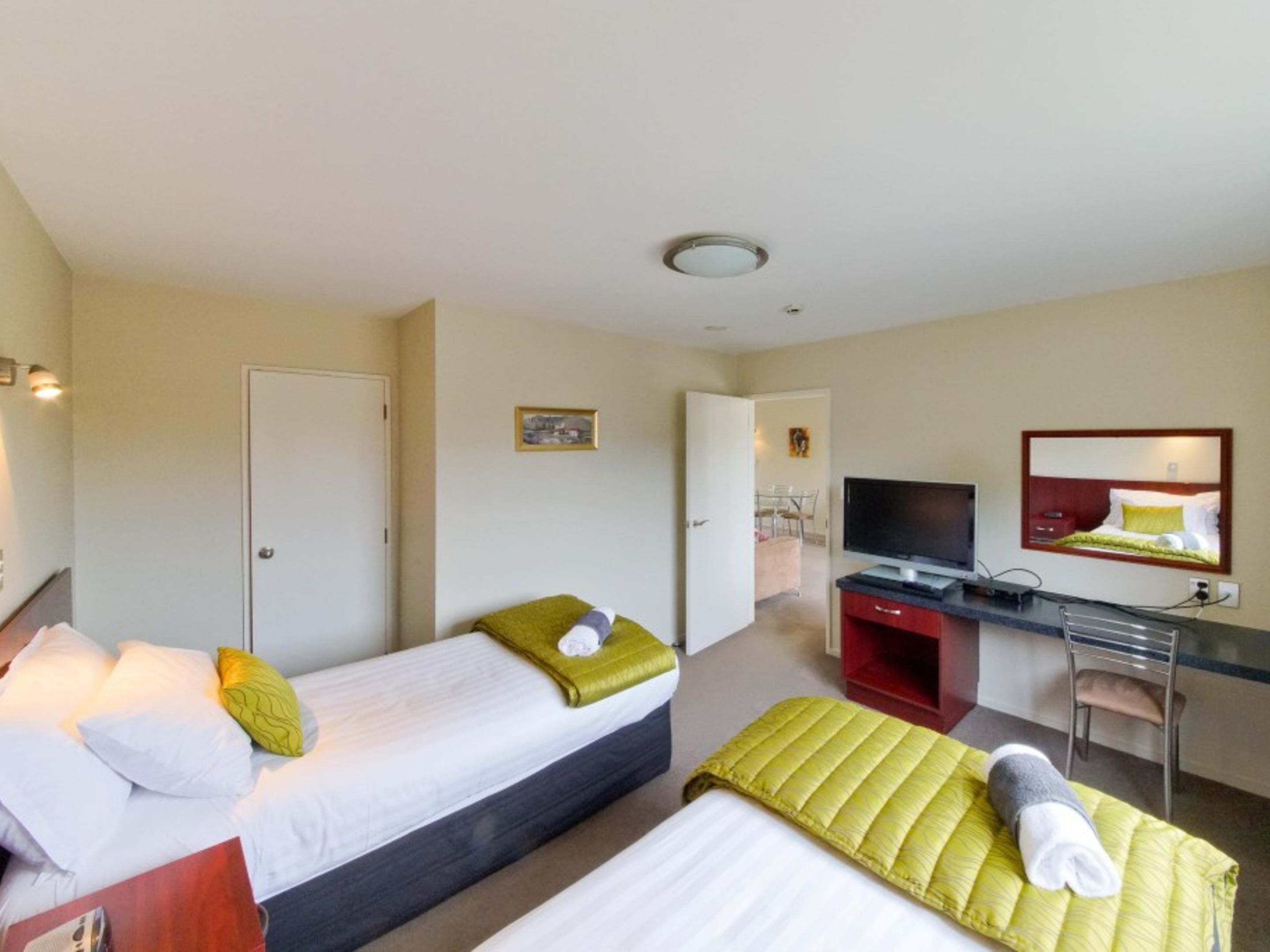 A hotel room with two beds, a desk, a TV, and a mirror.