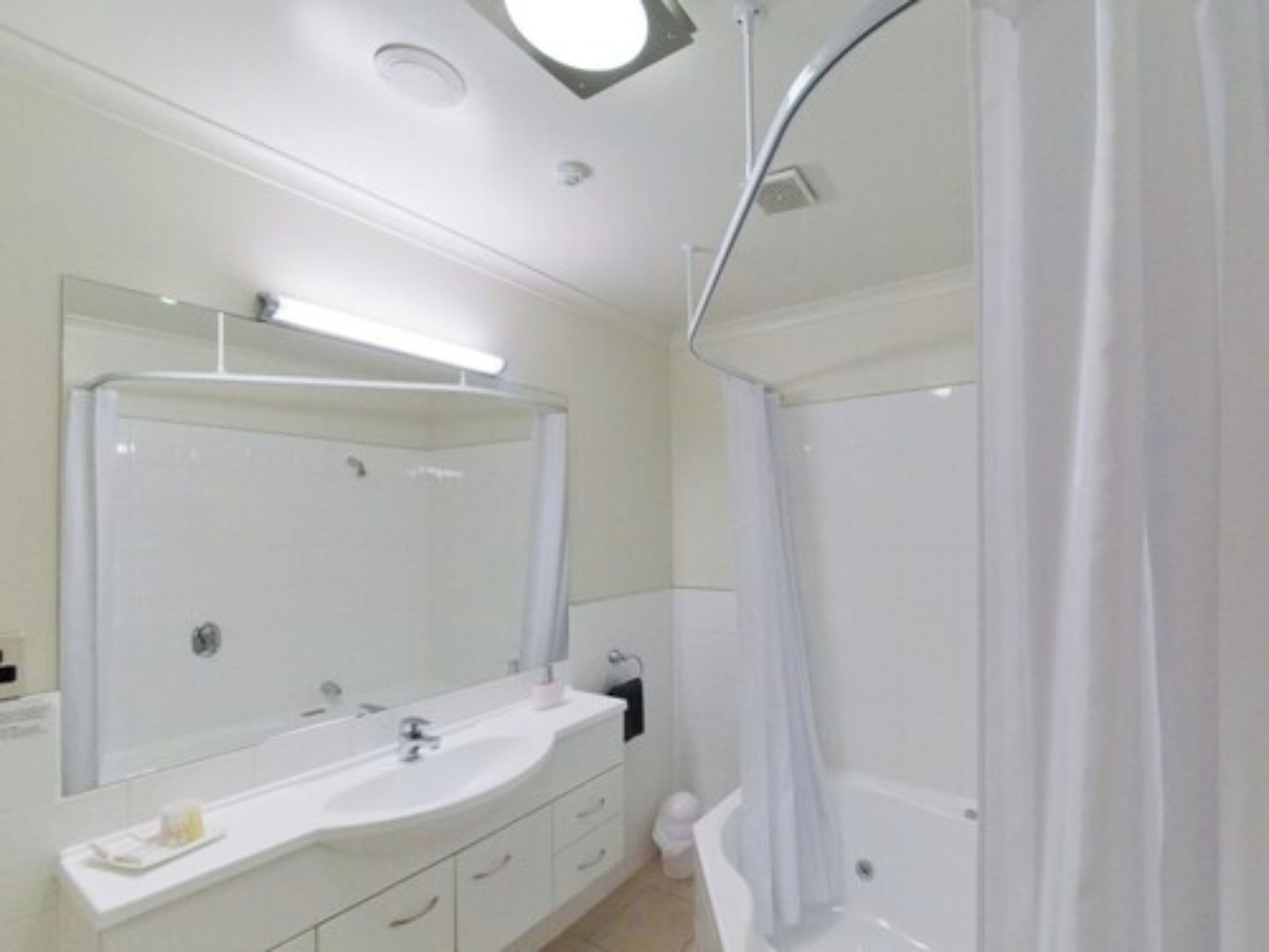 A modern bathroom with a large mirror, a white sink, a bathtub, and a shower curtain.