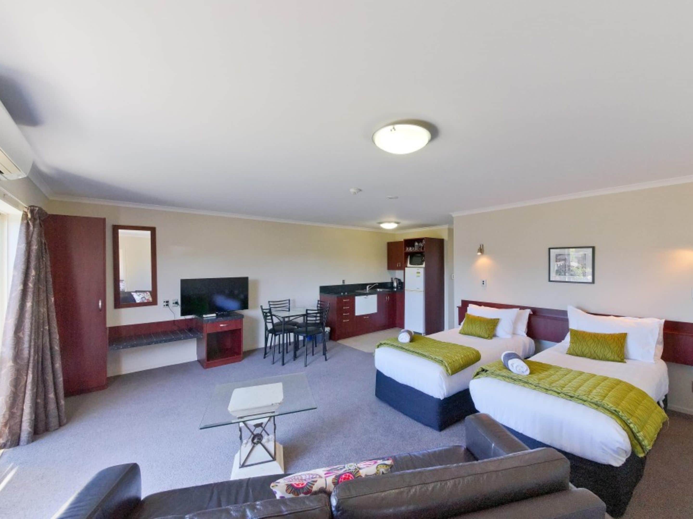 A hotel room with two beds, a desk, a TV, a small table, and a sofa.