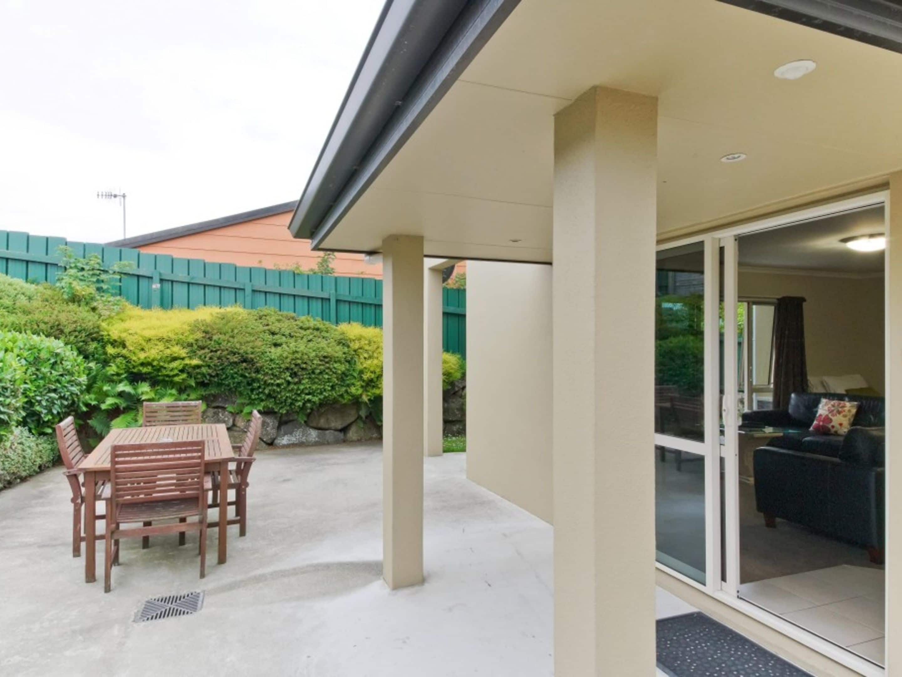 A covered patio with a table and chairs, a sliding glass door leading to a living room with a sofa and a coffee table.