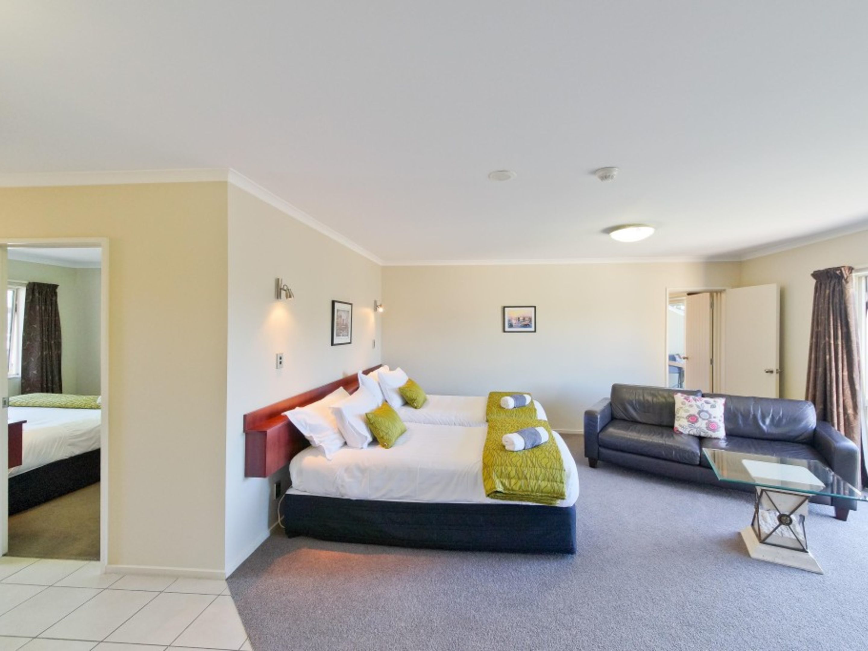 A hotel room with a large bed, a sofa, a glass coffee table, and a view of the outside.