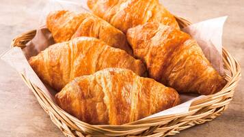 A basket of golden-brown croissants on a wooden surface.