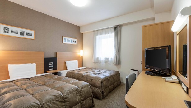 Ein Hotelzimmer mit zwei Betten, einem Schreibtisch mit Fernseher und gerahmten Bildern an der Wand.