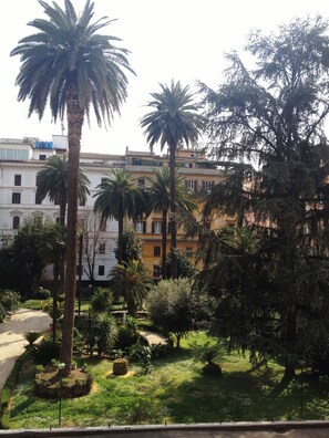 A courtyard with palm trees, a gravel path, and buildings with balconies in the background. - Capitolium Rooms (Rome)